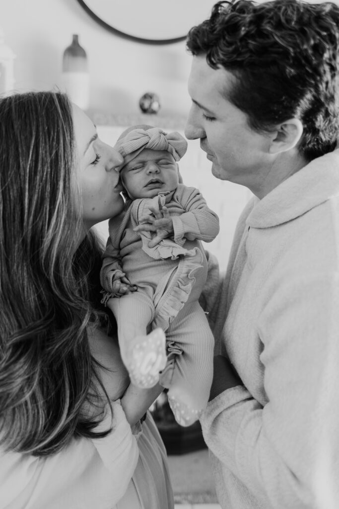new parents holding baby giving a kiss during newborn photography session