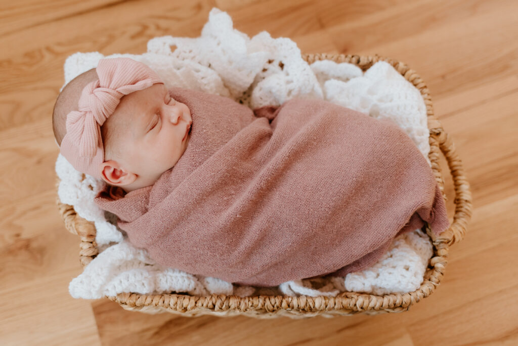 newborn baby in basket in pink swaddle
