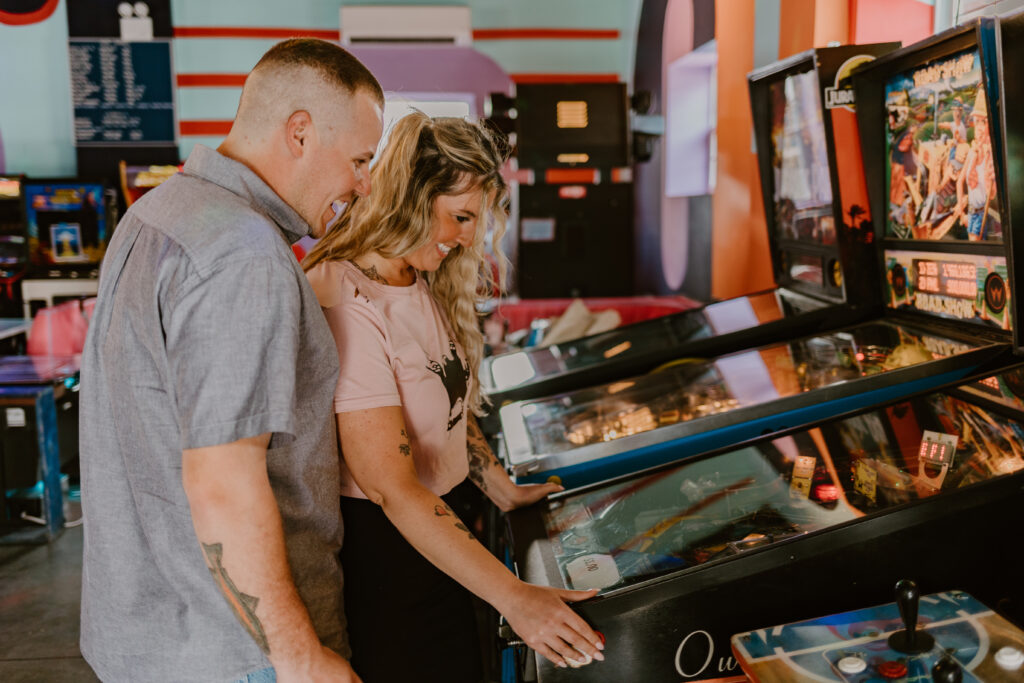 Engaged couple playing at an arcade machine, enjoying the playful and nostalgic atmosphere.