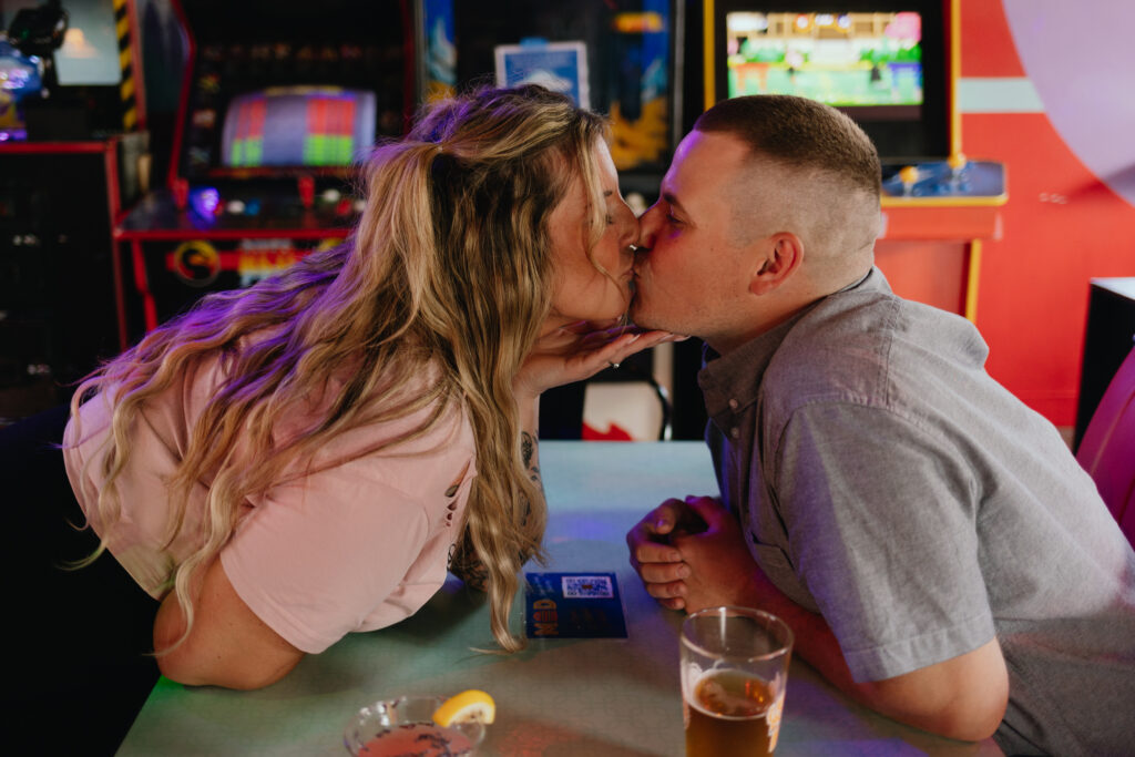 Intimate moment of a couple seated at the bar in Happy Valley Arcade, Beacon, sharing a moment of affection amid the retro setting.