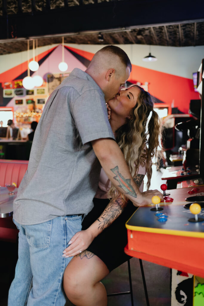 Engaged couple closely interacting over a tabletop arcade game, captured in a candid, intimate moment at Beacon's Happy Valley.