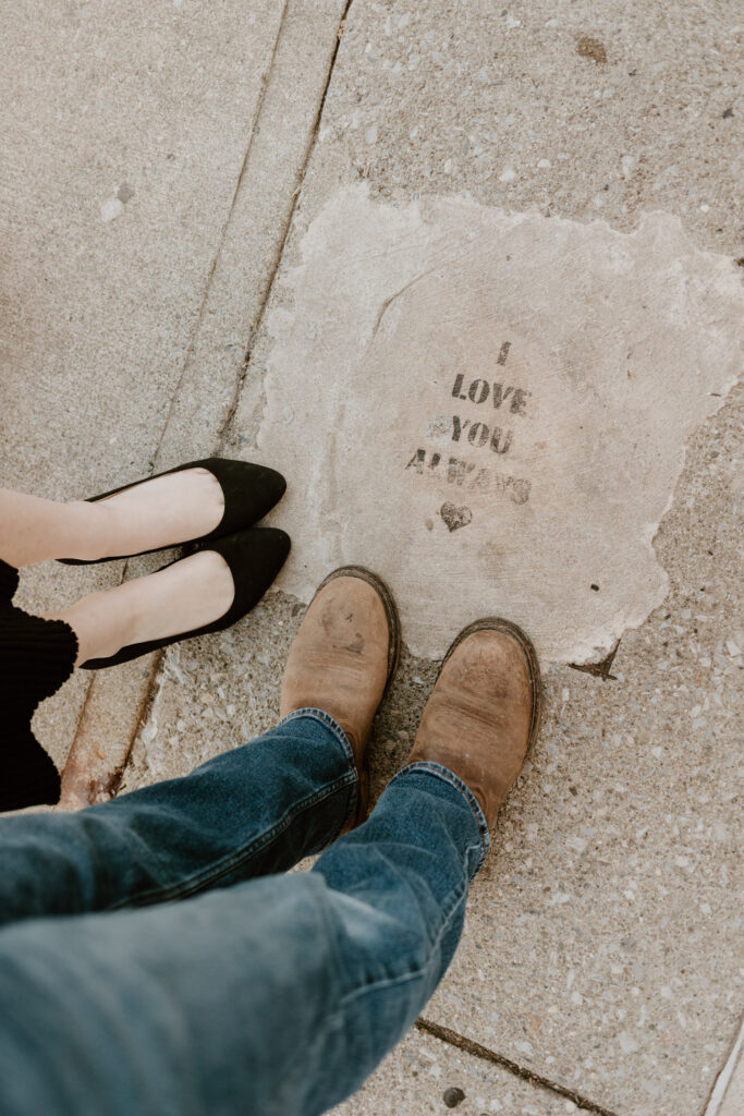 Candid shot of a couple's feet beside a heartfelt 'I Love You' message etched on a Beacon NY sidewalk, symbolizing romance in everyday places.