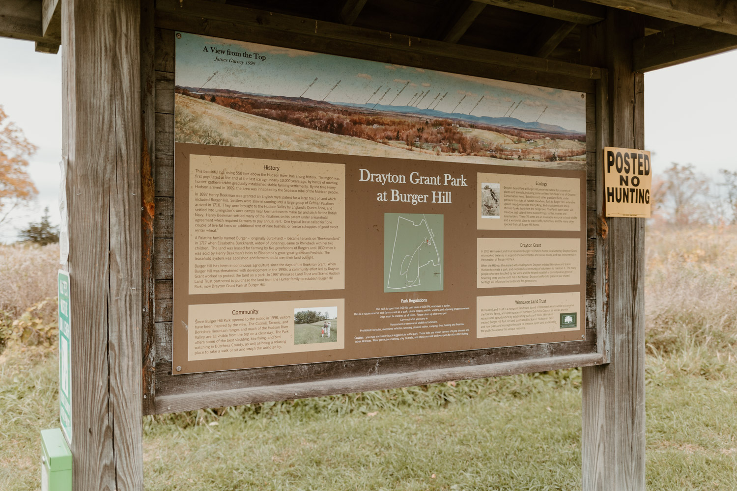 An informational sign at Drayton Grant Park at Burger Hill detailing the park's history, ecology, and community involvement, with an overview image of the landscape at the top and a "Posted No Hunting" sign to the right.