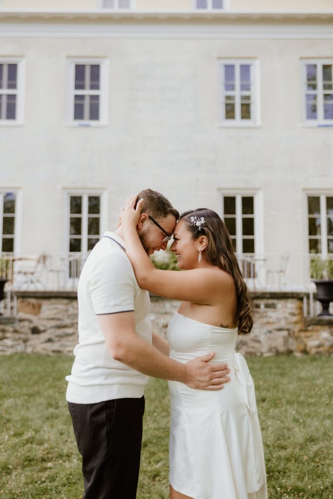 A couple embracing and touching foreheads while smiling in front of the Home of Franklin D. Roosevelt in Hyde Park, captured by a Hudson Valley family photographer.