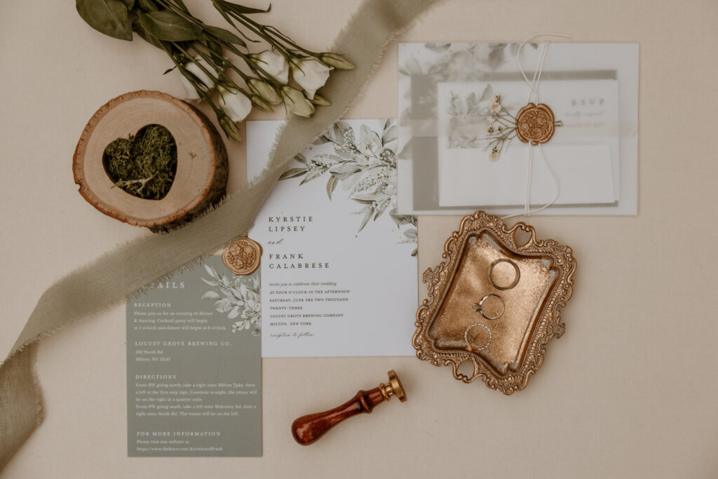 Elegant wedding invitation suite for Kyrstie and Frank's wedding at Locust Grove Brewing Company, featuring a wax seal, rustic wood and floral accents, and vintage-inspired ring holder.