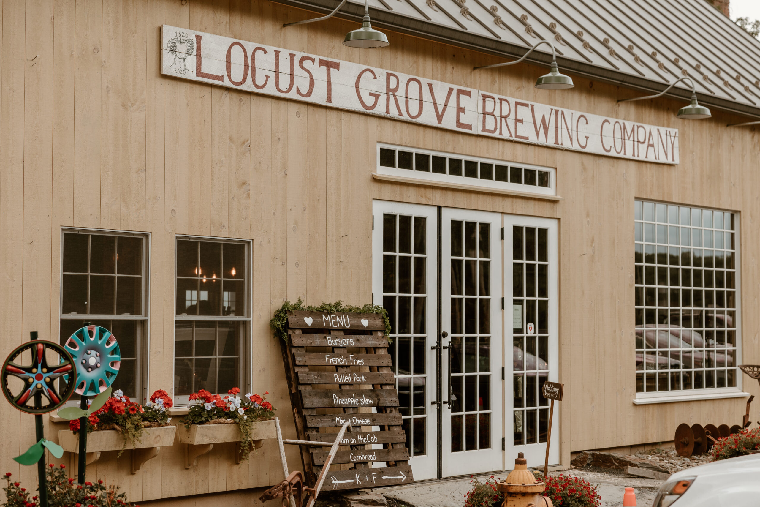 Exterior of Locust Grove Brewing Company with a rustic wooden façade, vintage wheel decorations, and a menu board displaying casual dining options.