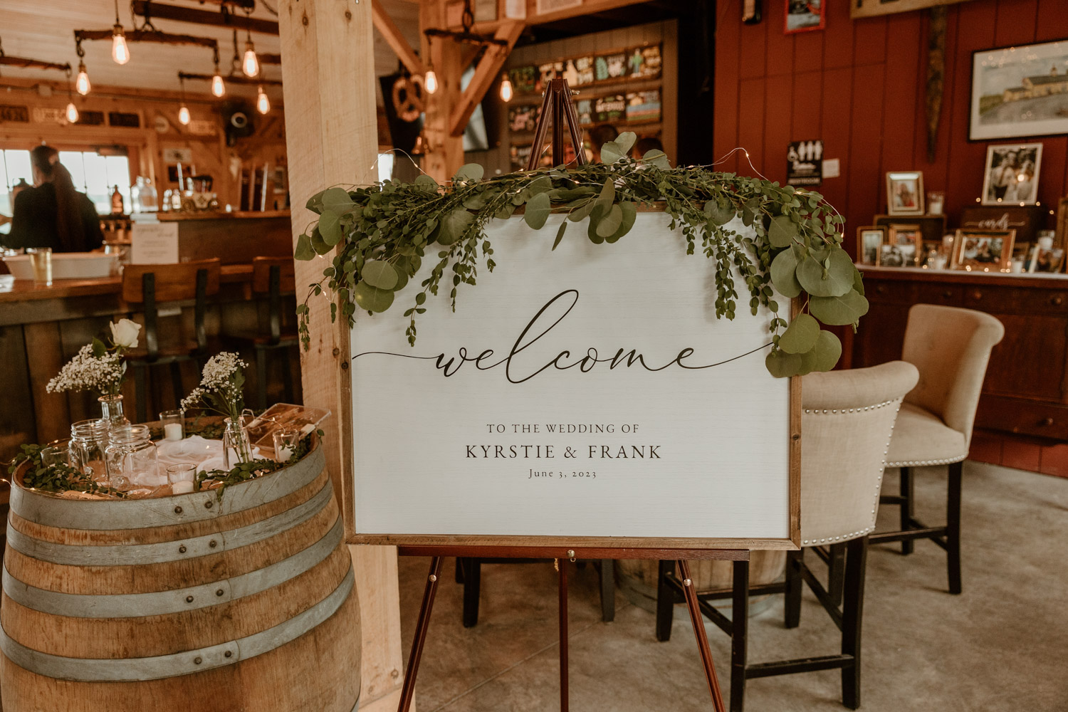 Chic wedding welcome sign adorned with fresh eucalyptus, inviting guests to the union of Kyrstie & Frank at Locust Grove Brewing Company.