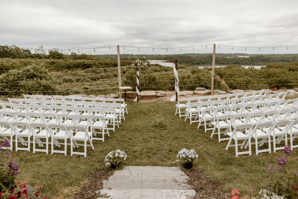 Serene outdoor wedding setup at Locust Grove Brewery with rows of white chairs facing an elegant wooden arch.