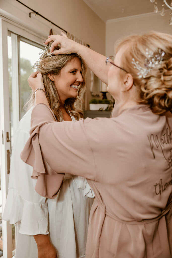 Mother of the bride placing a delicate tiara on her daughter's head, sharing a joyous smile on the wedding day at Locust Grove.