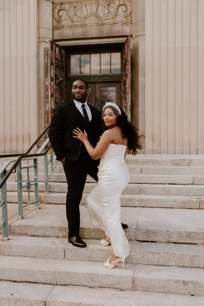 Elopement celebration at Rockland County Courthouse with a bride playfully posing with her groom on the steps, showcasing their style and the iconic courthouse doors.
