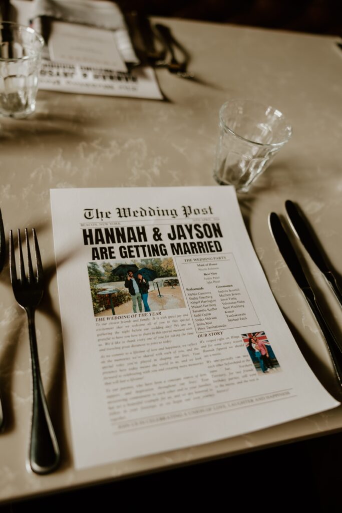 A detailed 'Wedding Post' newspaper-style menu placed on a table setting at Wonderbar. The menu announces 'Hannah & Jayson Are Getting Married' and includes a cute couple photo, details about the wedding party, and their love story, enhancing the dining experience with a personal touch.