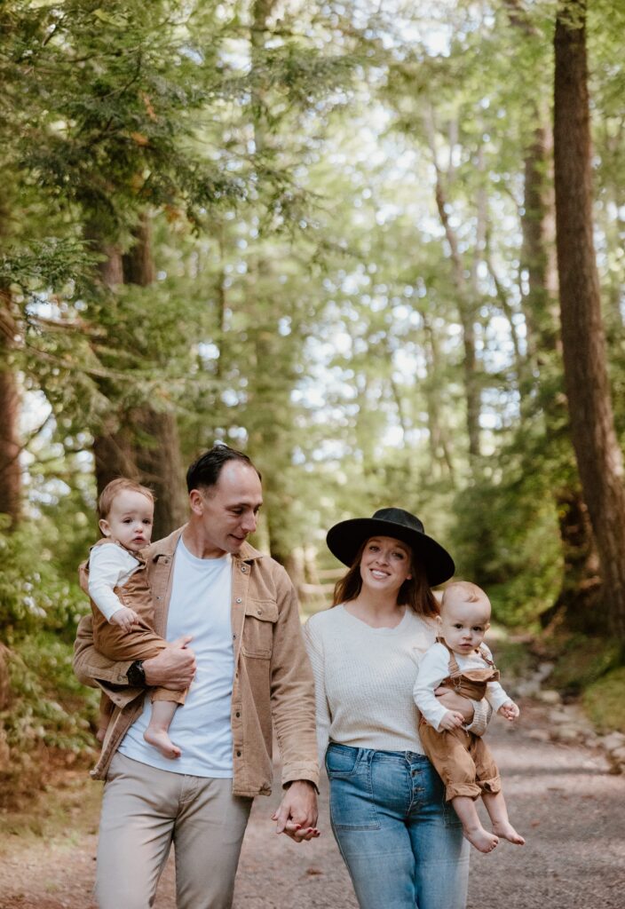 Parents and their two babies walking hand-in-hand through a tranquil Hudson Valley forest path.