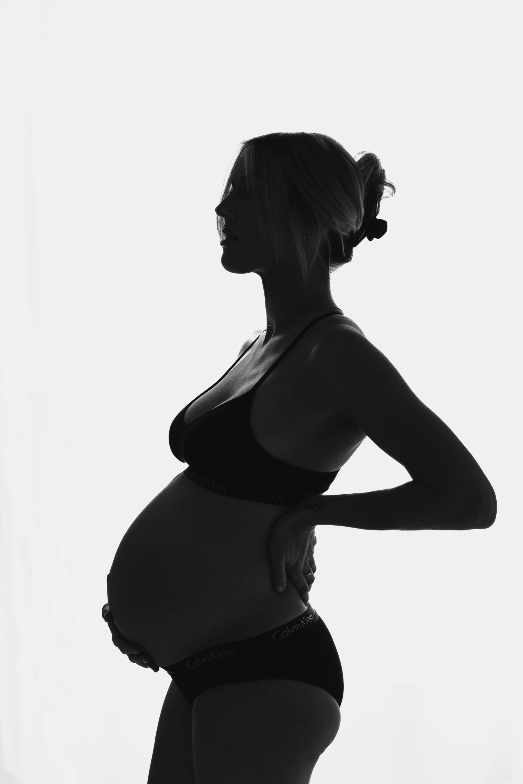 Silhouette of a pregnant woman in black undergarments, highlighting her baby bump in an elegant maternity photoshoot.