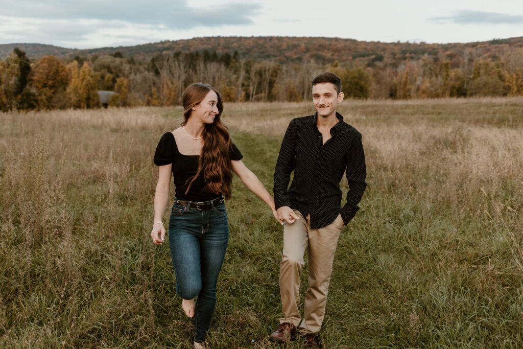 Couple walking hand-in-hand through a scenic hidden field in Pawling, NY, during their engagement session.