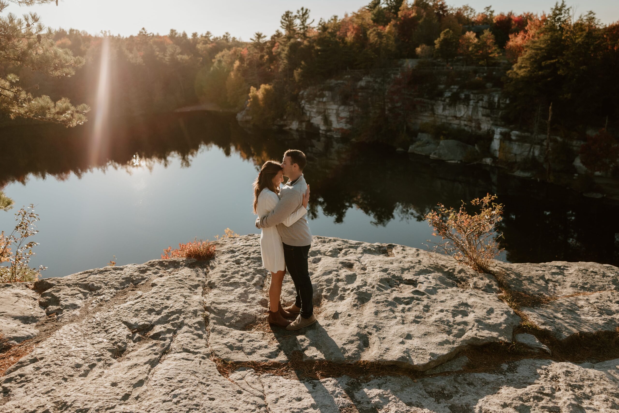 Engaged couple embracing on a rocky cliff overlooking Lake Minnewaska during golden hour in the Hudson Valley.