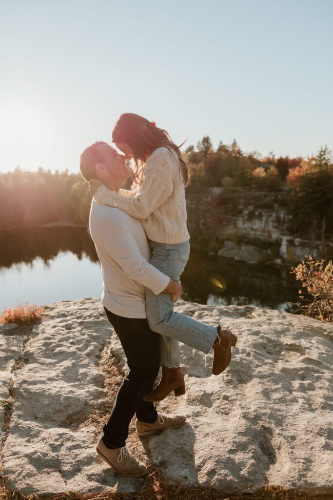 A couple shares a joyful moment as the man lifts his partner during a romantic sunset engagement session at Lake Minnewaska.