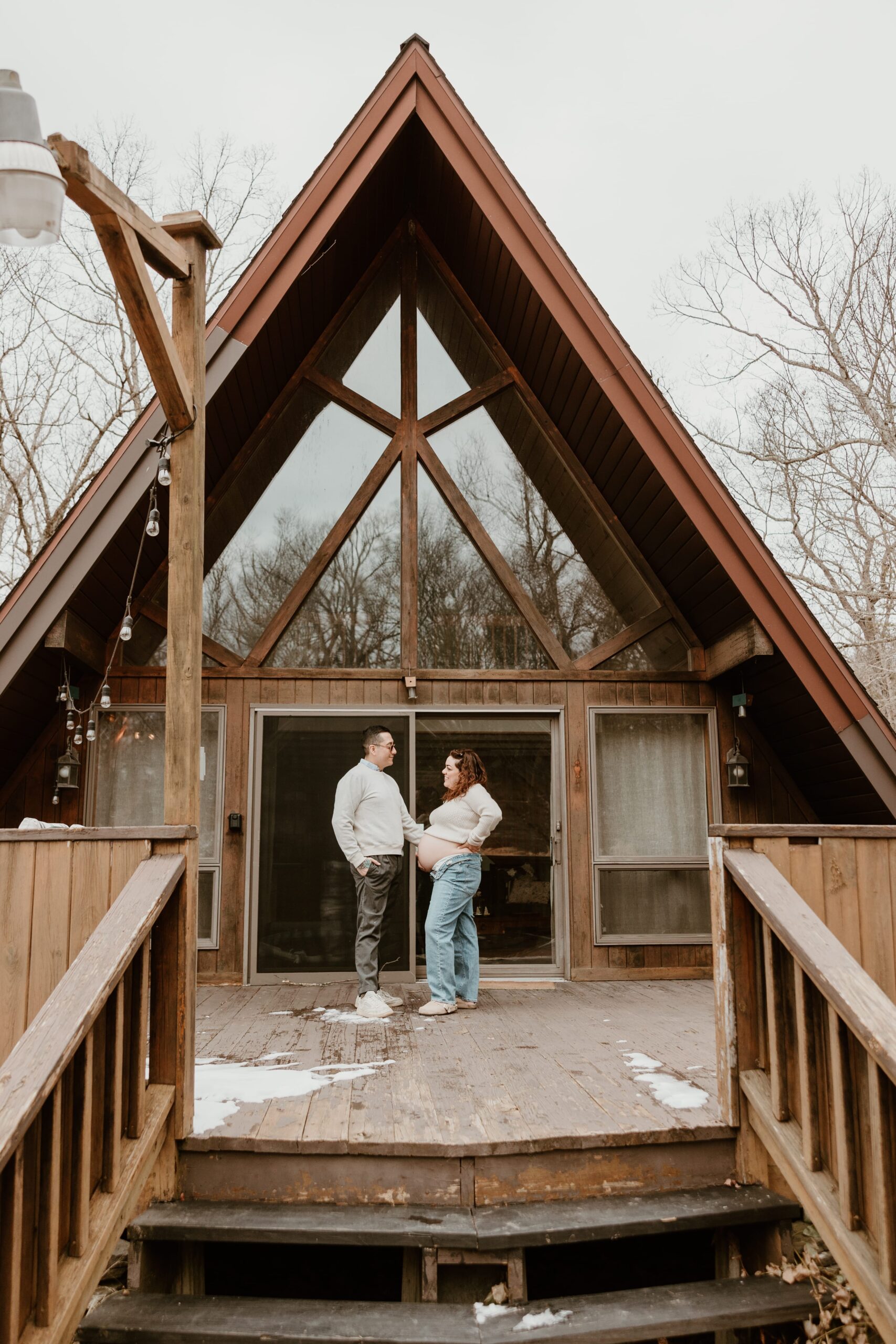 A maternity session featuring a couple standing on the deck of an A-frame Airbnb, capturing a cozy and intimate moment in a rustic setting.