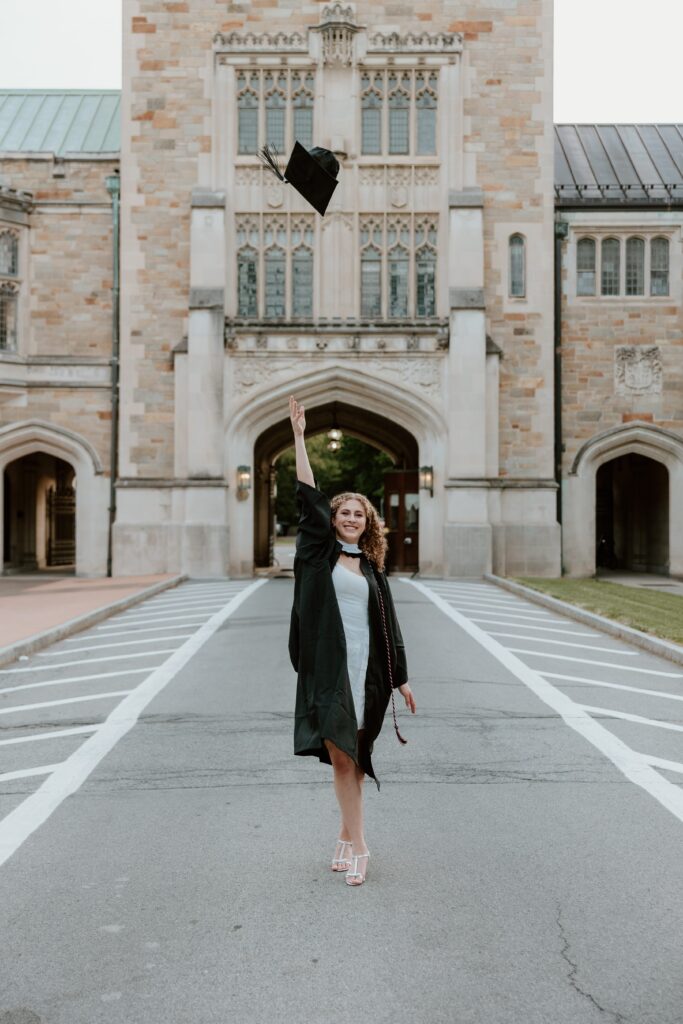 Graduate tossing graduation cap on Vassar College campus during evening photo session.