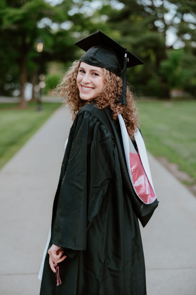 Graduate in cap and gown smiling over shoulder during Vassar College graduation photo session.