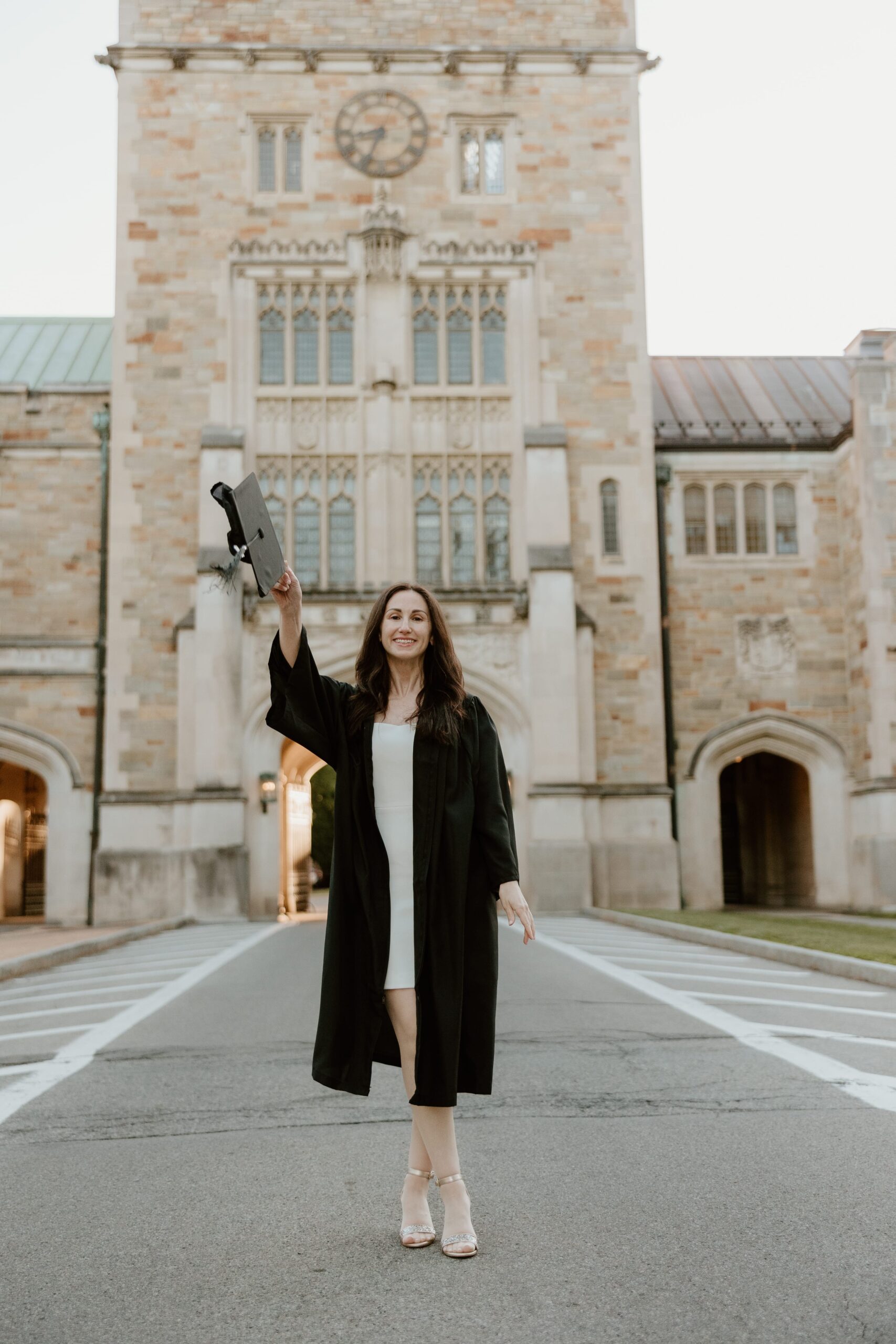 Graduating student holding up her cap while smiling in front of the Vassar College library building during her senior photo session in Poughkeepsie, NY.