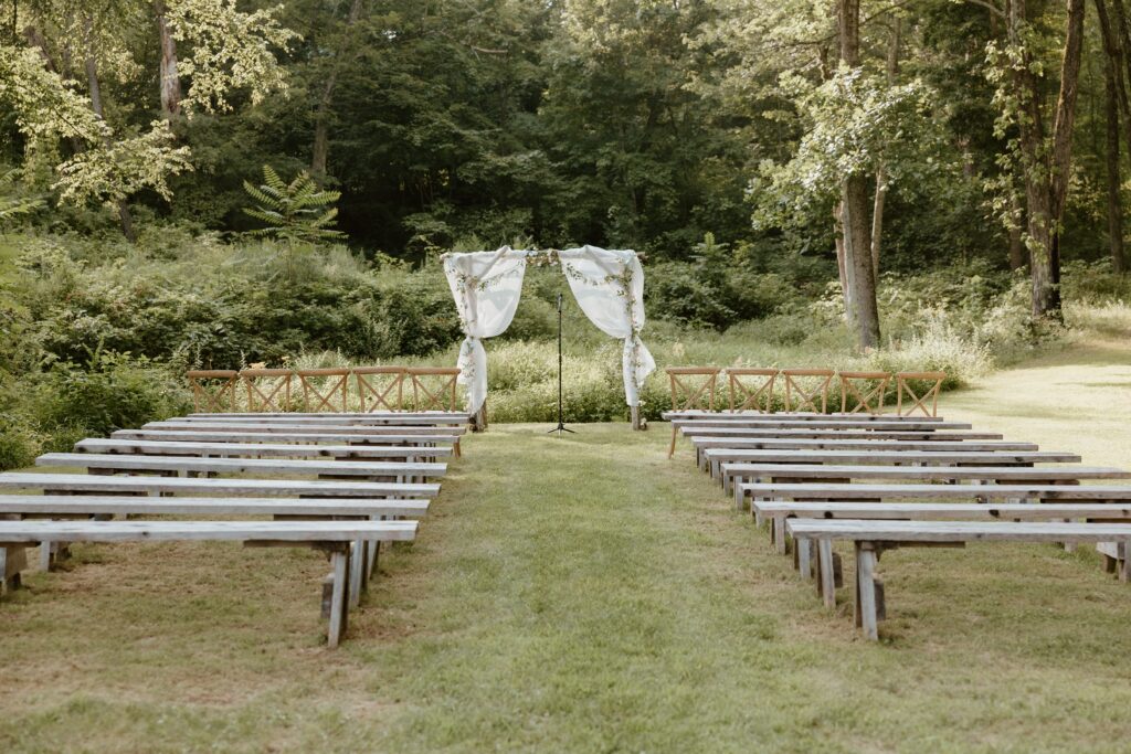 Outdoor ceremony setup at Stonehill’s Farmhouse in Accord, NY with rustic benches and draped floral arch.