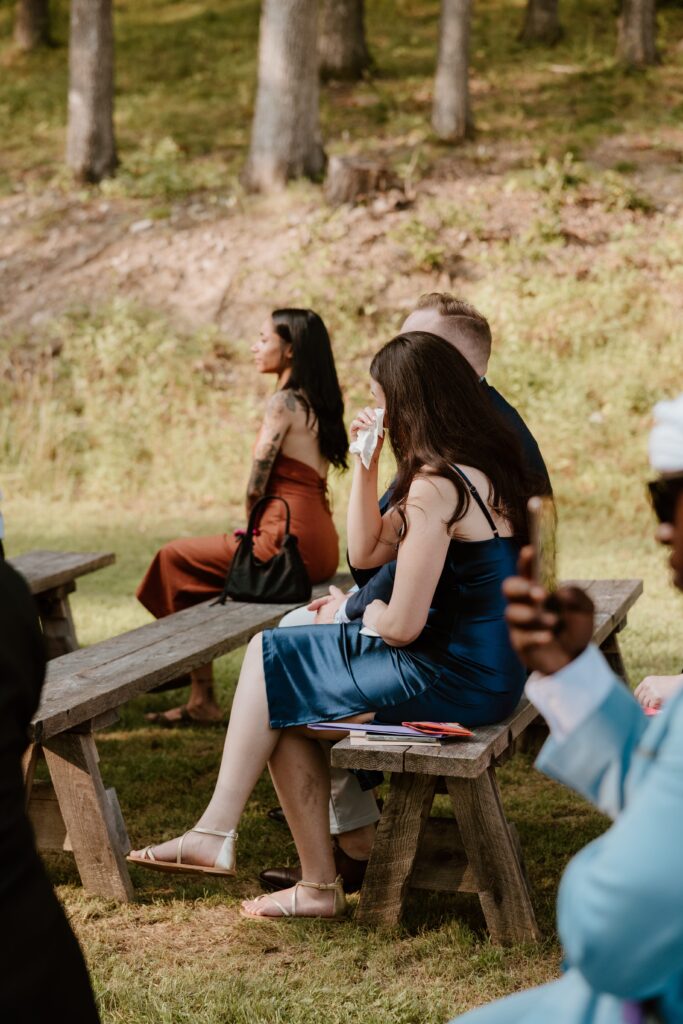 Wedding guest wiping away tears during outdoor ceremony.