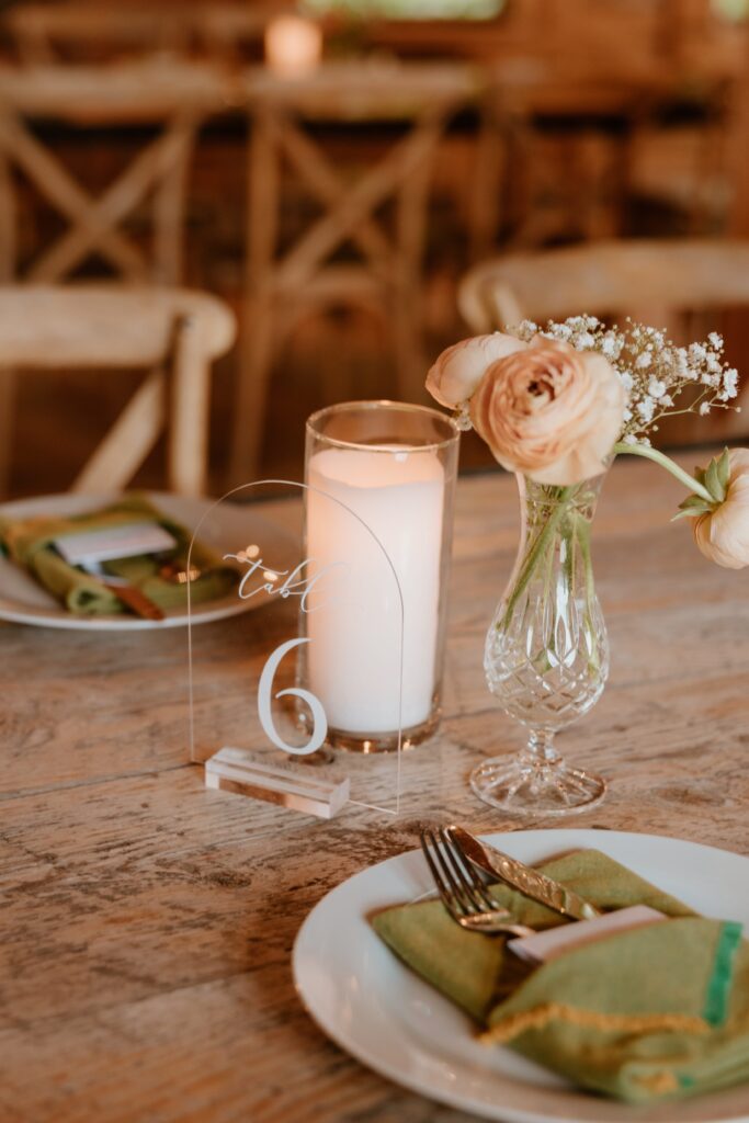 Wedding reception table with candle, blush ranunculus flowers, and modern acrylic table number.