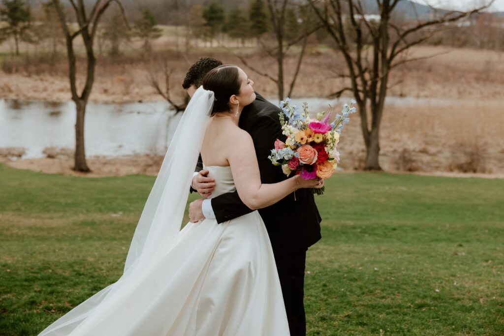 Bride and groom embracing by the water during wedding portraits