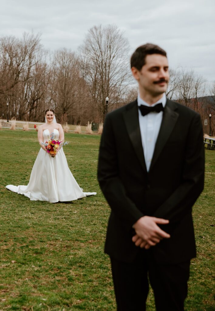 Bride walking toward groom during their first look on a grassy field