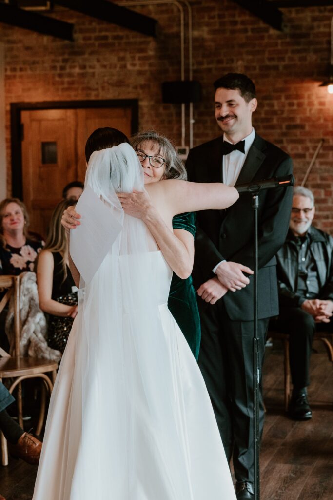 Emotional moment during wedding ceremony as bride hugs a family member at Drowned Lands Brewery in Warwick NY