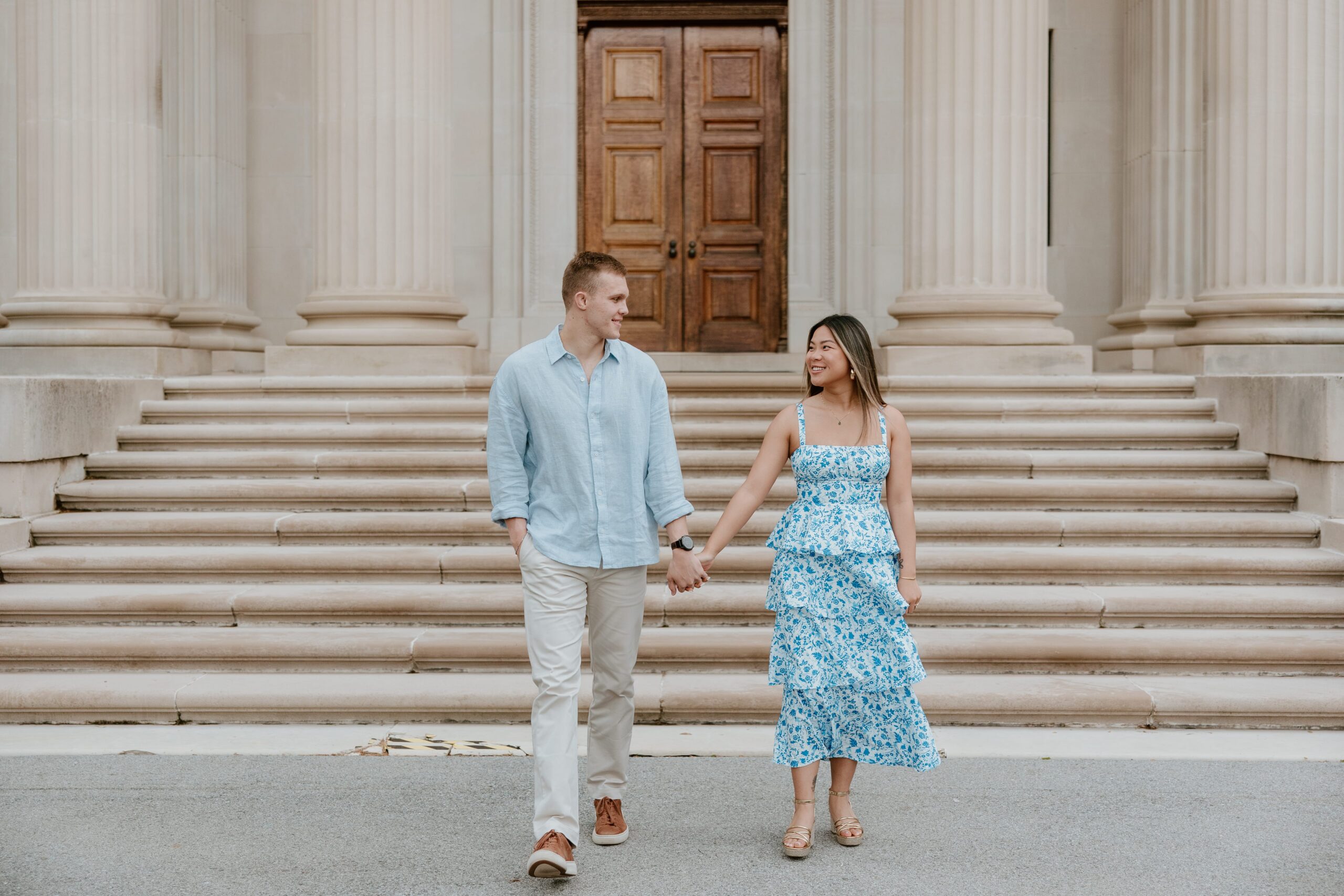 Couple holding hands on the front steps of Vanderbilt Mansion during an engagement session in Hyde Park, New York.