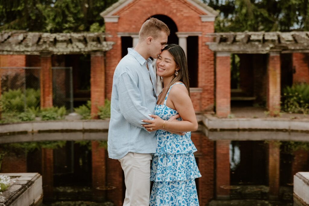 Engaged couple embracing in front of the reflection pool at Vanderbilt Mansion during an engagement session in Hyde Park, NY.