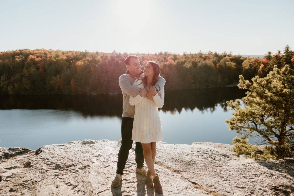 Couple posing by Lake Minnewaska during a fall engagement session in the Hudson Valley with colorful autumn foliage in the background.